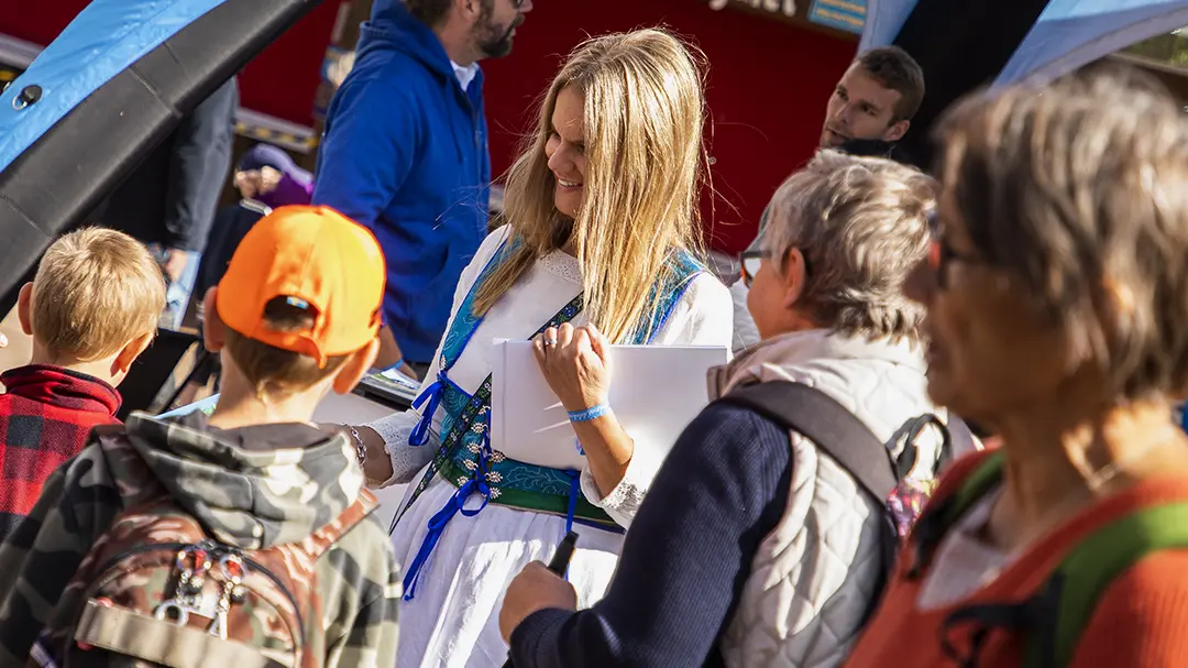 Kvinna i Dalakraftdräkt delar ut skattkartor till barn på Leksand Sommarland